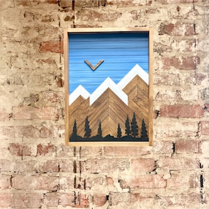 May include: A wooden wall art piece depicting a mountain range with a blue sky and white snow-capped peaks. The mountains are made of wood and the sky is painted blue. There are trees in the foreground.