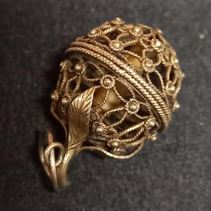Peut inclure: Pendentif en forme d'œuf en filigrane doré orné d'un motif floral et de feuilles. Le pendentif présente un travail ajouré complexe et est suspendu à une bélière décorative. Un bijou unique.