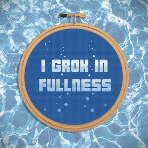 May include: A blue embroidery hoop with the text "I GROK: IN FULLNESS" in white. The hoop is against a blue and white water background.