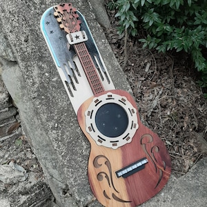 May include: A wooden guitar-shaped wall mount with a cutout for a smart speaker. The mount is decorated with a patriotic American flag design and has a wood grain finish.