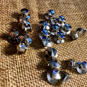 May include: A close-up of a group of silver-toned safety pins with blue accents. The pins are scattered on a brown burlap surface.