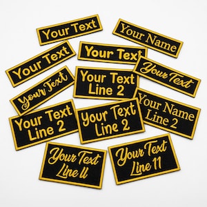 May include: Several black rectangular patches with gold embroidered text, including phrases such as "Your Text" and "Your Name." The patches, edged in gold, are scattered on a white surface. The text also includes "Line 2" and "Line 11".