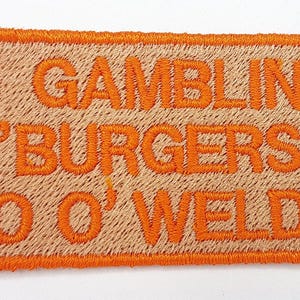 a patch with the text "J GAMBLING "BURGERS" CEO O'WELLING" embroidered on it.
