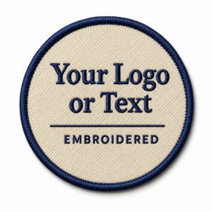 May include: A circular embroidered patch featuring a cream-coloured fabric base with a dark blue stitched border. The text "Your Logo or Text" is embroidered in dark blue, followed by a horizontal line and the word "EMBROIDERED" below it.
