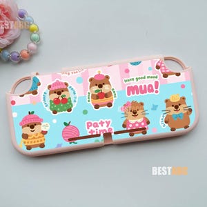 May include: A light pink protective console case featuring a light blue and pink striped background with cartoon otters, cherries, and the text "Have good mood mua!" and "Paty time". The case has cutouts for buttons and joysticks.
