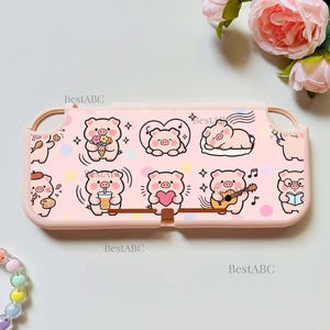 May include: A light pink protective console case featuring a repeating pattern of cartoon pigs in various activities, including holding flowers, drinking bubble tea, playing guitar, and sleeping, with small stars and colorful polka dots throughout.
