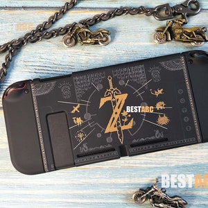 K&ouml;nnte beinhalten: Schwarze Nintendo Switch-H&uuml;lle mit goldenem Zelda-Design. Das Design zeigt ein Schwert, einen Schild und andere Symbole aus dem Spiel. Die H&uuml;lle ist aus strapazierf&auml;higem Kunststoff und hat ein weiches Innenfutter zum Schutz Ihrer Konsole.