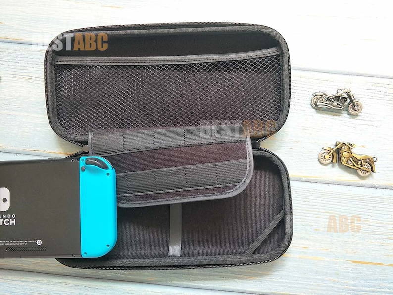 K&ouml;nnte beinhalten: Eine schwarze Tragetasche mit Rei&szlig;verschluss und einem Netzfach im Inneren. Die Tasche ist ge&ouml;ffnet und eine blau-schwarze Nintendo Switch-Konsole befindet sich darin. Die Tasche liegt auf einer hellblauen Oberfl&auml;che.