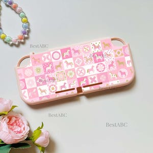 May include: A light pink gaming console protective case featuring a repeating grid pattern of white, pink, and gold horses, geometric shapes, and circular motifs. The case includes cutouts for buttons and ports, with the text BestABC printed on it.
