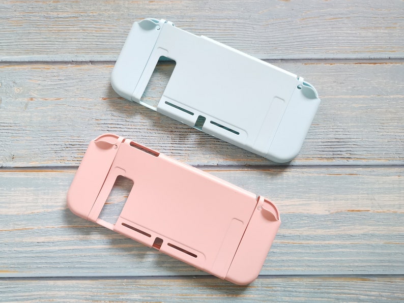 May include: Two protective cases for a Nintendo Switch console. One case is light blue and the other is pink. Both cases have cutouts for the buttons and joysticks.