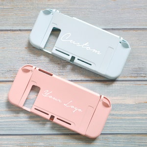 May include: Two Nintendo Switch game cases, one light blue with the word "Custom" and one pink with the words "Your Logo".