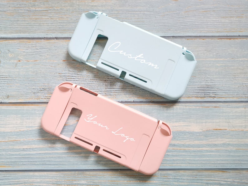 May include: Two Nintendo Switch game cases, one light blue with the word "Custom" and one pink with the words "Your Logo".