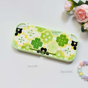 May include: A light green protective console case featuring a repeating pattern of four-leaf clovers in shades of white, lime green, and black against a yellow background. The text BestABC is printed multiple times across the surface of the case.