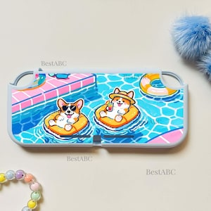 May include: A white protective gaming console case featuring a colorful graphic of two Corgi dogs floating in a blue swimming pool on orange inner tubes. One dog wears sunglasses and the other wears a straw hat while holding a drink. Text reads BestABC.