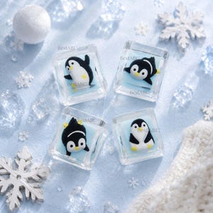 May include: Four square clear resin keycaps, each featuring a small black and white penguin figurine embedded in a light blue base. The text BestABC is printed on each keycap. The penguins are depicted in various poses, including standing and swimming.