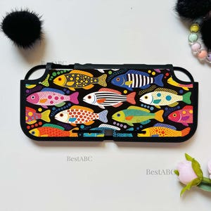 May include: A black protective gaming console case featuring a vibrant, multi-colored pattern of various fish. The fish are depicted in shades of yellow, pink, blue, orange, and green with polka dot and striped designs against a black background.