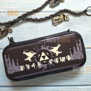 K&ouml;nnte beinhalten: Schwarze Nintendo Switch-Spieleh&uuml;lle mit einem wei&szlig;en Design, das ein dreieckiges Symbol, einen Drachen und ein Schloss zeigt. Die H&uuml;lle hat einen Rei&szlig;verschluss.