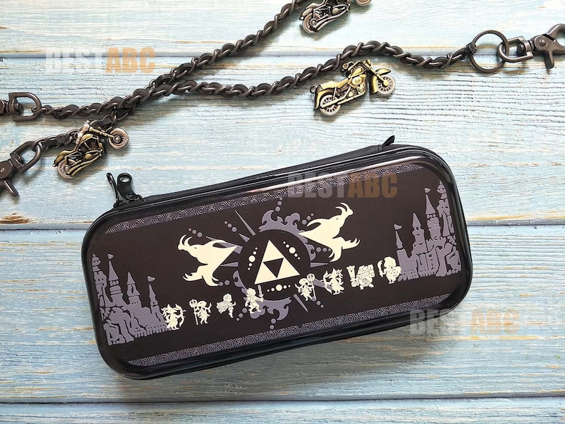 K&ouml;nnte beinhalten: Schwarze Nintendo Switch-Spieleh&uuml;lle mit einem wei&szlig;en Design, das ein dreieckiges Symbol, einen Drachen und ein Schloss zeigt. Die H&uuml;lle hat einen Rei&szlig;verschluss.