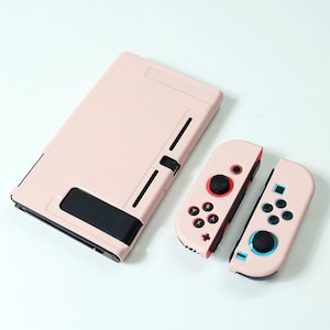 May include: A pink Nintendo Switch console case with a black trim and two pink Joy-Con controllers. The controllers have red and blue buttons.