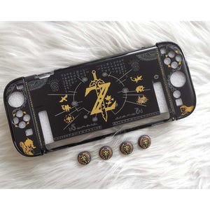 May include: Black Switch case with gold detailing, featuring a Zelda theme. The case has a gold sword and the letter Z in the centre. Includes four matching thumb grips.