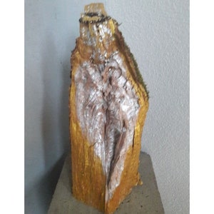 Puede incluir: Una escultura de madera con una textura rugosa y natural. La madera está pintada de oro y blanco, creando un contraste llamativo. La escultura tiene la forma de una torre alta y estrecha con una punta puntiaguda.
