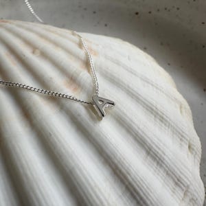 May include: A silver necklace with a small letter A pendant. The necklace is on a white seashell background.