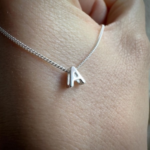 May include: A silver necklace with a small, silver letter 'A' pendant.