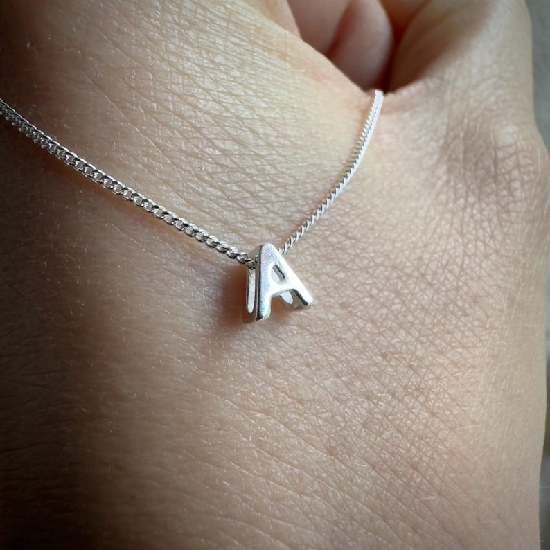 May include: A silver necklace with a small, silver letter 'A' pendant.