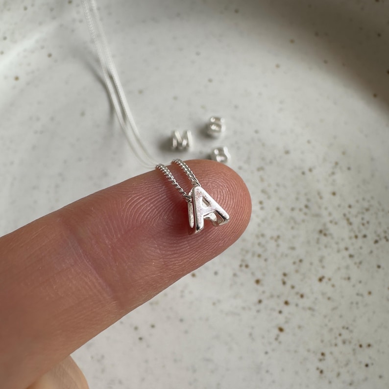 May include: A silver necklace with a small, three-dimensional letter 'A' charm.