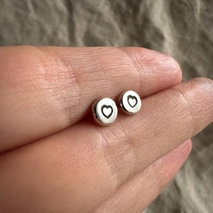 Op de afbeelding: Een paar zilveren oorbelletjes met een hartvormig ontwerp. De oorbelletjes zijn klein en delicaat.