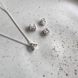 May include: A silver necklace with a silver letter A charm. There are also silver letter charms for the letters M, S, and B.