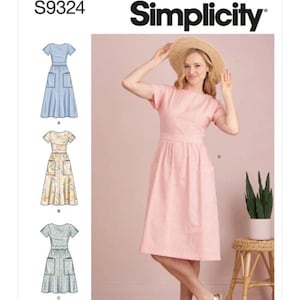 May include: A Simplicity sewing pattern package, S9324, showing a pink gingham dress with short sleeves and pockets. The package also shows illustrations of similar dresses in blue and patterned fabrics. The text "Designed and printed in USA" is visible.