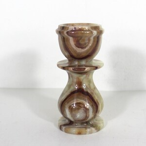 May include: A decorative candlestick holder made of layered onyx stone. The holder features a cup-shaped top, a circular base, and a bulbous midsection. The stone has brown, tan, and cream-colored bands.