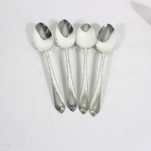 May include: Five silver teaspoons with ornate handles. The spoons are arranged in a row, with the handles pointing towards the top of the image.