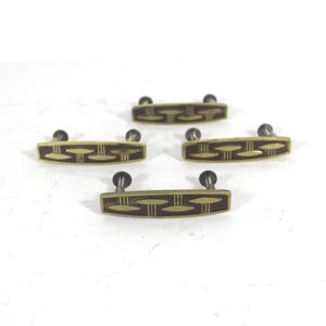 Peut inclure: Quatre poignées de tiroir de cabinet ton or avec un motif en émail brun. Chaque poignée a une forme rectangulaire aux bords arrondis et un motif géométrique subtil.