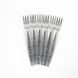 May include: Seven stainless steel forks with decorative floral patterns on the handles. The tines are sharp and evenly spaced. The forks are displayed on a white background.