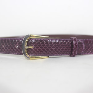 May include: A purple snakeskin-patterned belt with a silver and gold buckle. The belt is made of leather and features a single loop. A classic accessory, the belt is a deep shade of purple.