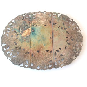 May include: A silver-plated, oval-shaped, decorative serving tray with an intricate, cut-out design. The tray is made of three sections that are hinged together.