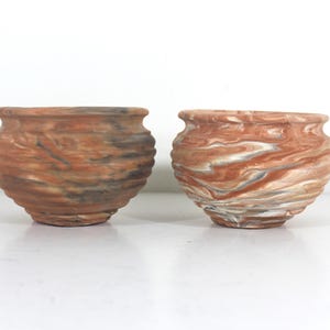 Peut inclure: Deux pots en terre cuite avec un glaçage marbré dans des tons de brun, blanc et gris. Les pots ont une forme arrondie et une lèvre légèrement évasée.