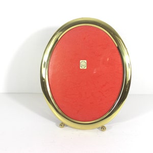 May include: A gold oval picture frame with a red velvet backing. The frame has a small label on the front that says "Made in Italy".