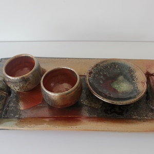 May include: A rectangular ceramic tray with two small bowls and a small dish. The tray has a brown, green, and black glaze. The bowls and dish have a similar glaze.