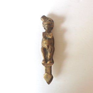 May include: A gold-coloured metal door knocker shaped like a monkey wearing a hat and bow tie.