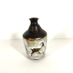 May include: A small, brown and white ceramic vase with a rounded body and a narrow neck. The vase has a mottled glaze with brown and white streaks.