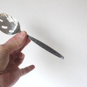 May include: A silver slotted serving spoon with an ornate floral design on the handle.