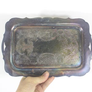 May include: A silver serving tray with an ornate, embossed design. The tray has a scalloped edge and a rectangular shape.