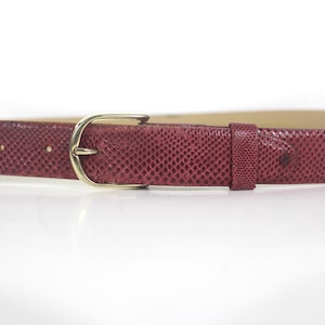 May include: A burgundy belt with a textured snakeskin pattern. It has a gold-coloured buckle and a matching belt loop. This belt is a stylish accessory for any outfit.
