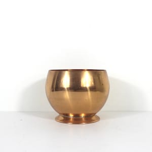May include: A shiny, gold-coloured metal planter with a rounded body and a flared base.