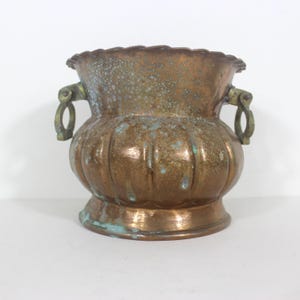 May include: A vintage bronze planter with a scalloped rim and two ornate handles. The planter has a bulbous body with vertical grooves and a weathered patina, showing hints of green oxidation. A decorative piece for home decor.