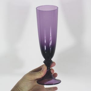 May include: A tall, clear glass champagne flute with a purple ombre gradient. The glass has a delicate stem and a wide base.