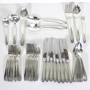 May include: A set of silverware in a silver finish. The set includes forks, knives, spoons, and serving pieces. The silverware has a floral design on the handles.